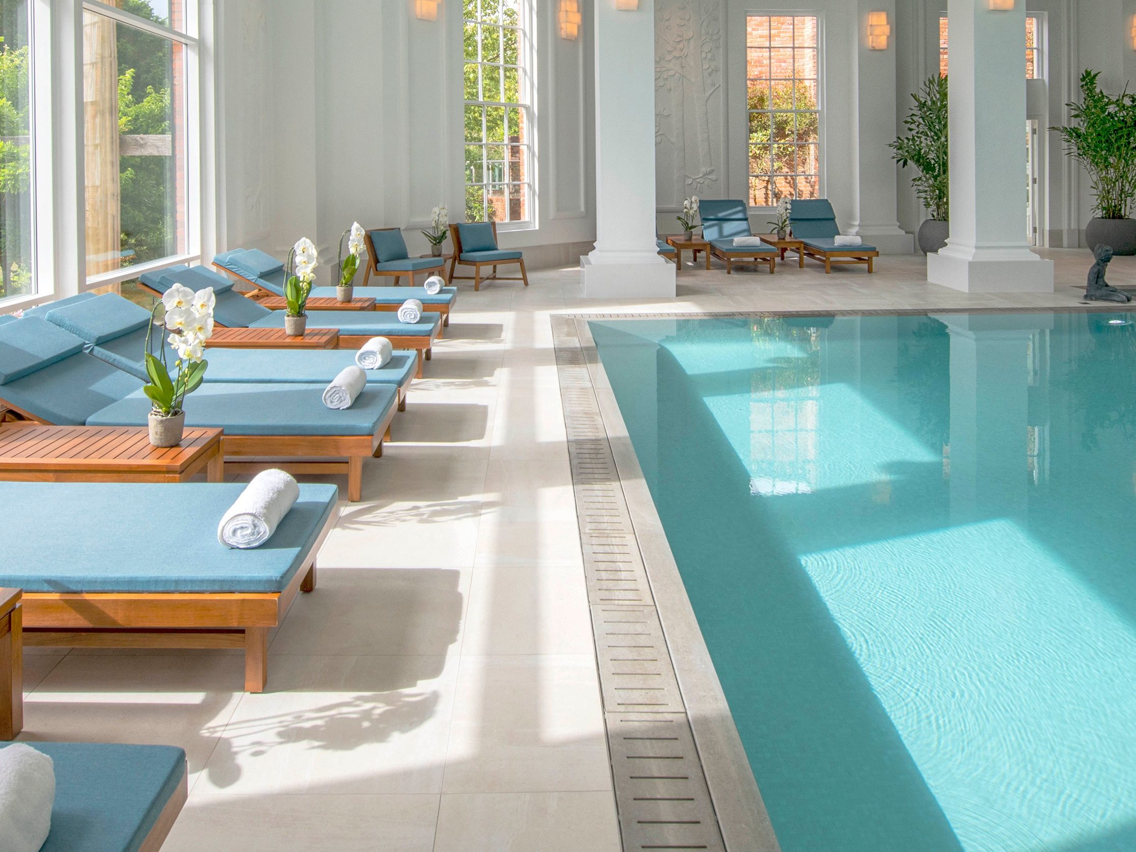 Chewton Glen pool with sun bed with light blue pillows with a white towel rolled nicely on the sun bed and a flower on each table